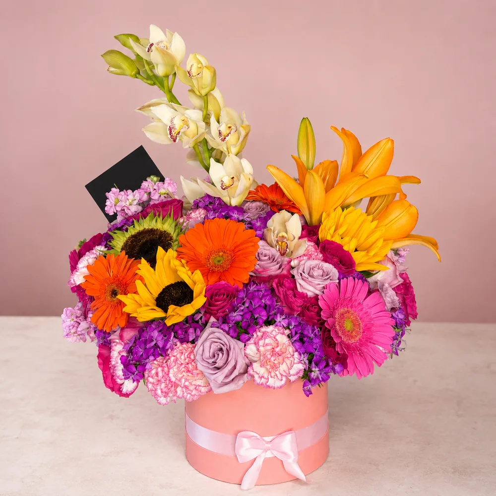 Jardín Encantado - Arreglo colorido en caja rosa con orquídeas, lirios, girasoles, gerberas y rosas lavanda