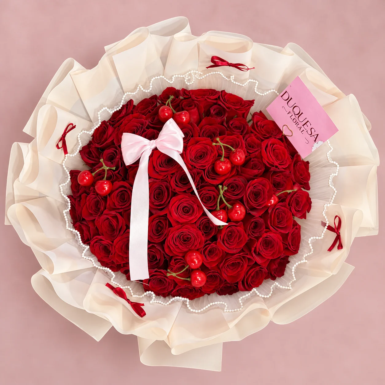 Cerezas de Amor - Ramo de 60 rosas rojas decorado con cerezas, perlas y moño rosado, envuelto en papel crema