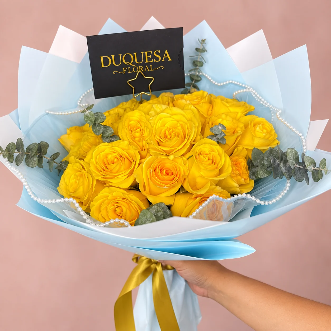 24 Rosas Amarillas - Ramo de 24 rosas amarillas con eucalipto y perlas, envuelto en papel celeste con lazo dorado