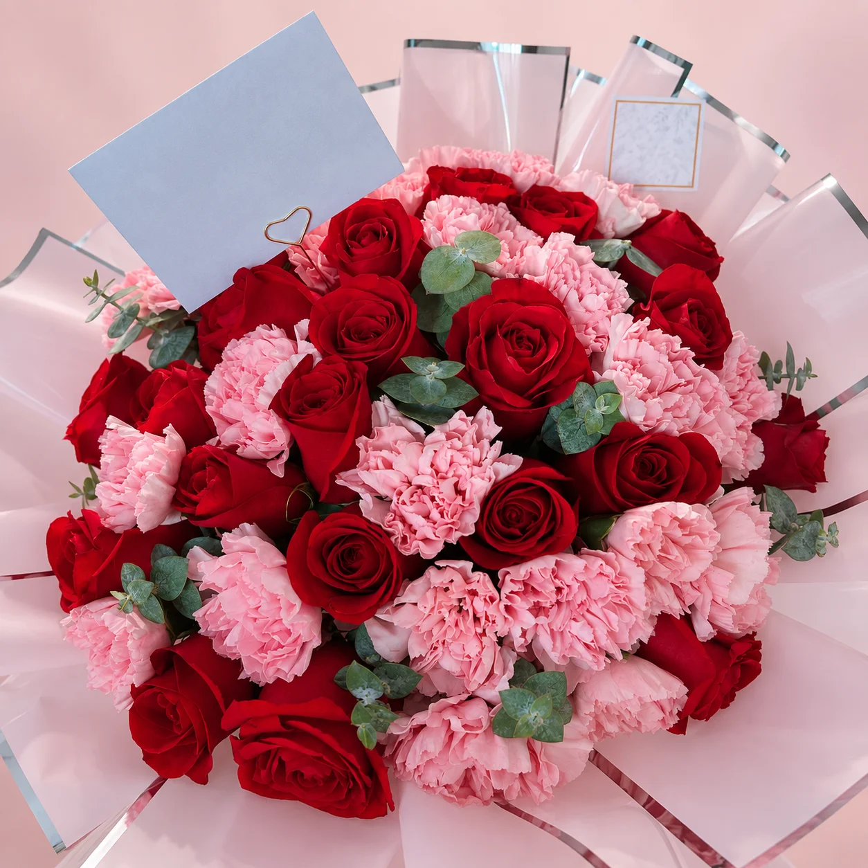 Rosas y Claveles - Ramo de 24 rosas rojas con claveles rosados y eucalipto, envuelto en papel rosa con borde plateado